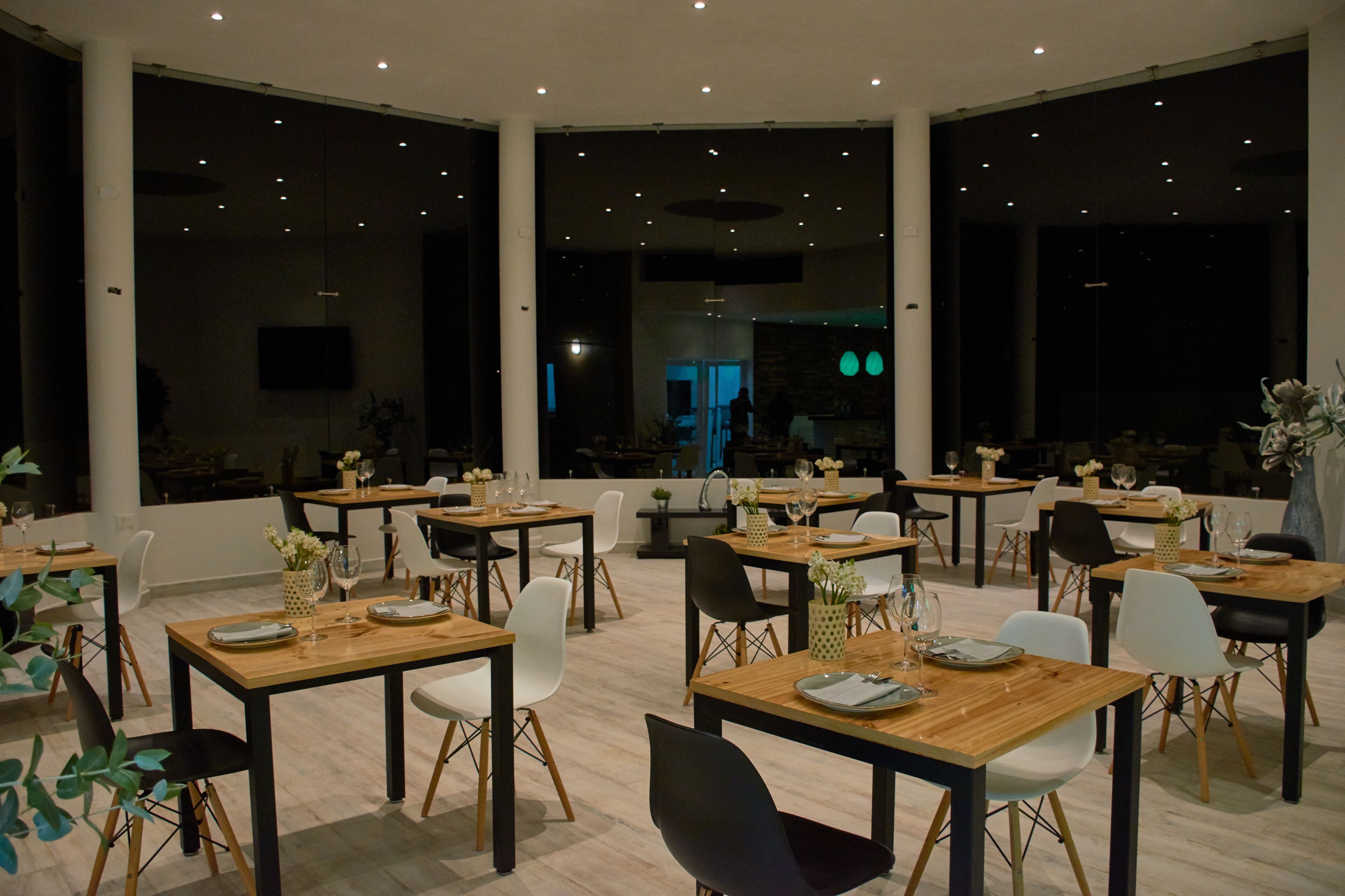 A spacious dining area with multiple tables and chairs, large windows, and a modern interior design.