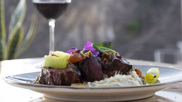 A plate of food with a glass of red wine and a mountain view in the background.
