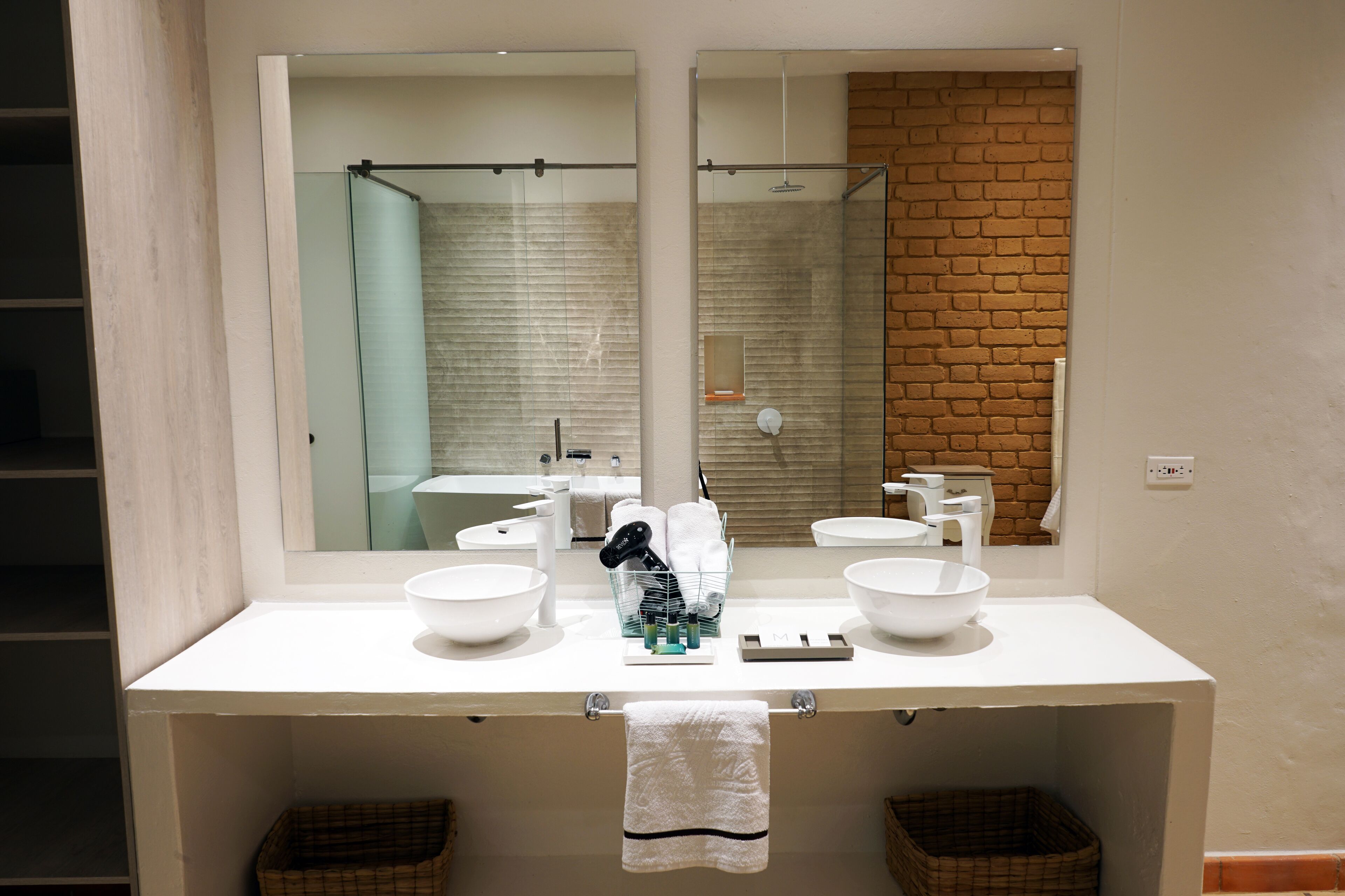 Une salle de bain avec un meuble-lavabo blanc, deux vasques, un miroir et un espace douche visible à travers la porte en verre.
