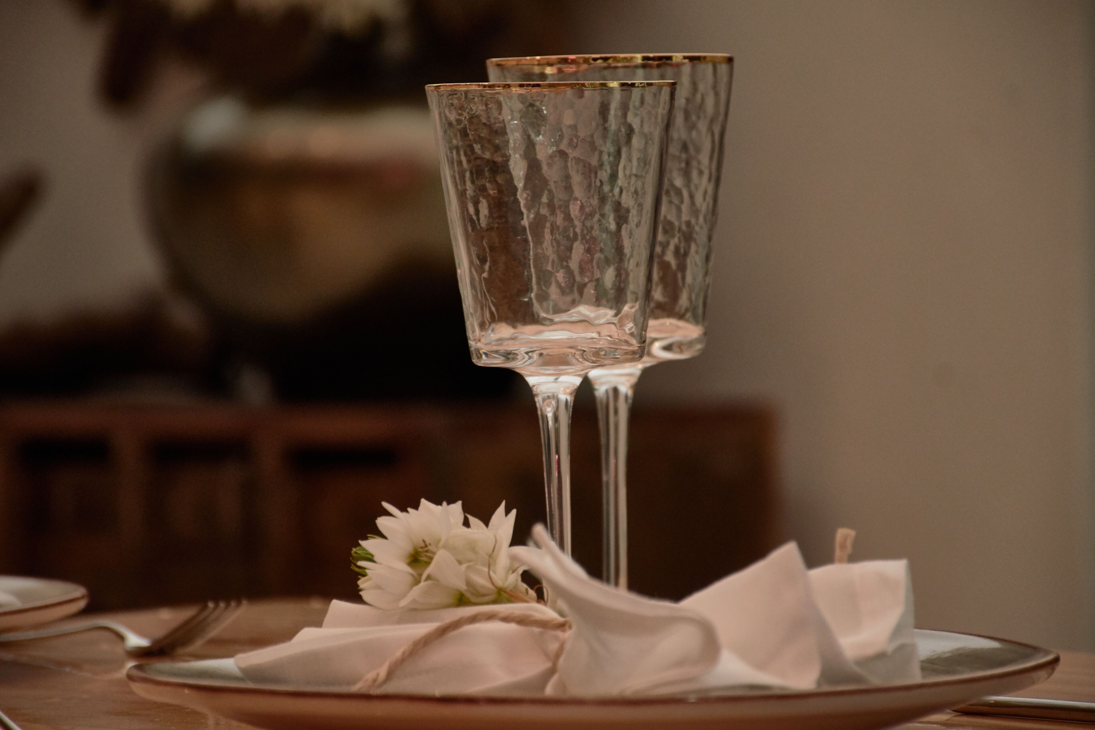 Una mesa dispuesta con una copa de vidrio transparente, una servilleta doblada y una pequeña flor blanca.