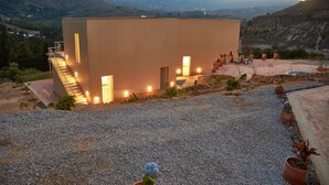 Un bâtiment moderne doté d’un toit plat, d’un escalier menant à l’entrée et d’une terrasse en gravier agrémentée de plantes en pot.