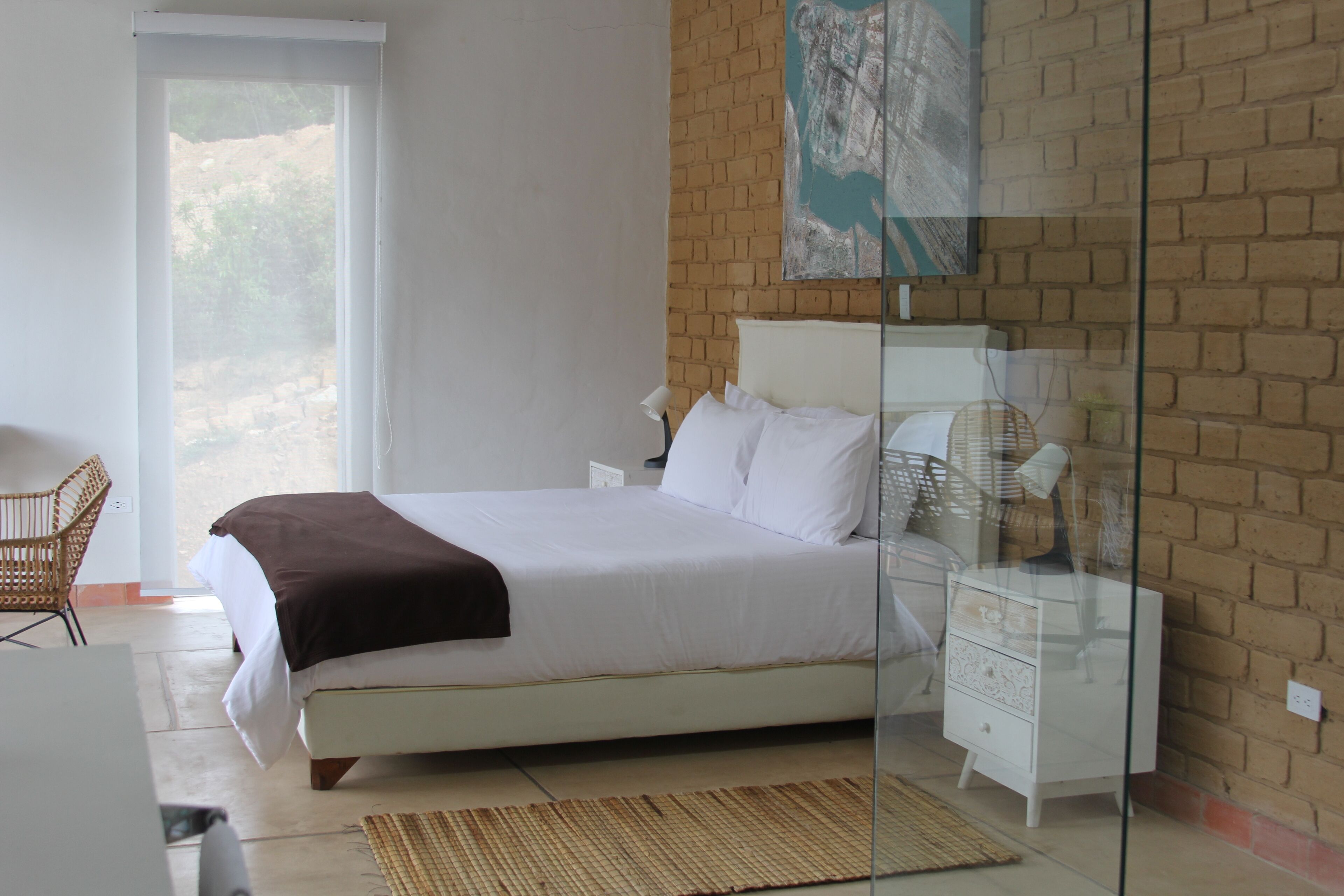 A bedroom with a bed, bedside tables, a chair, and a glass partition.