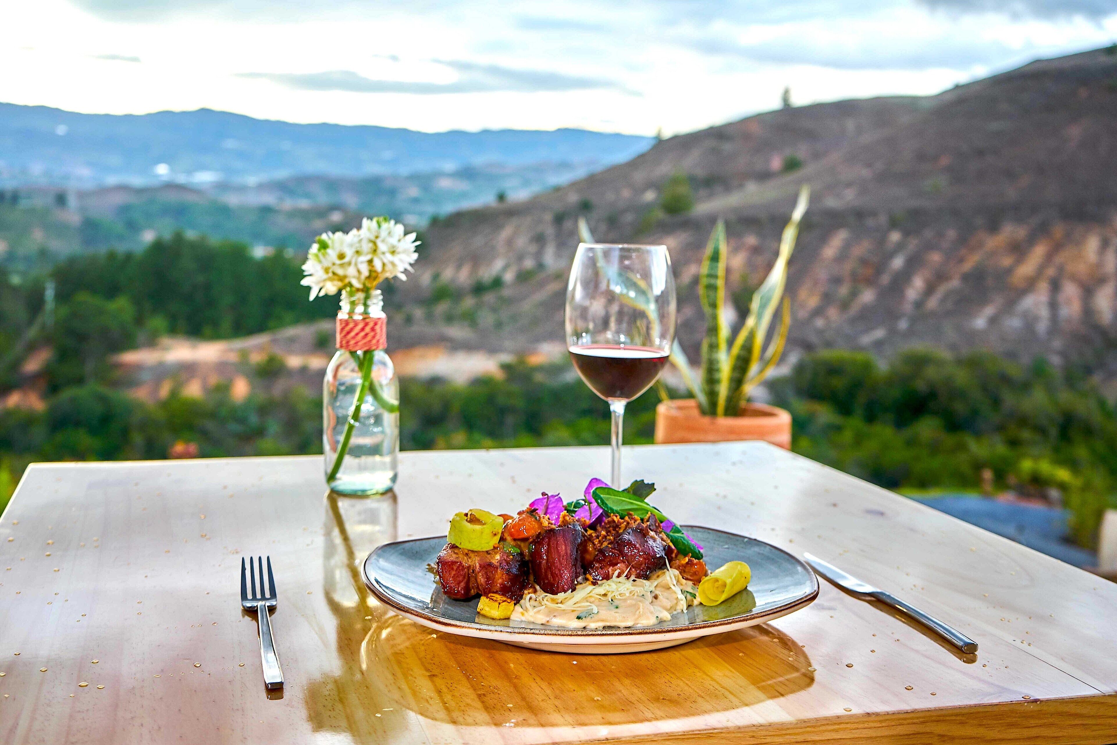 A dining table with a plate of food, a glass of red wine, and a vase of flowers.