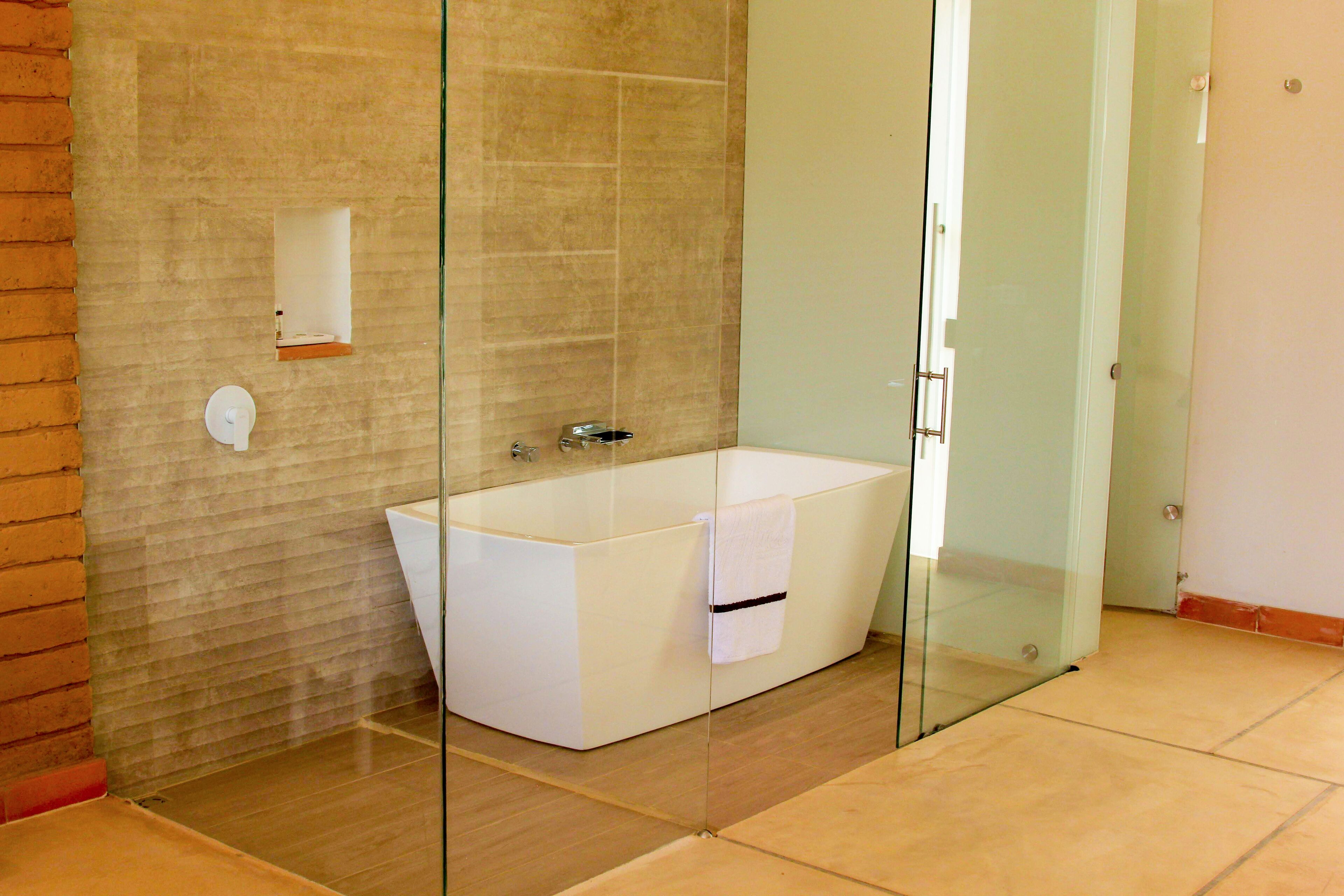 Un baño moderno con ducha envuelta en vidrio, bañera blanca y piso de baldosas.