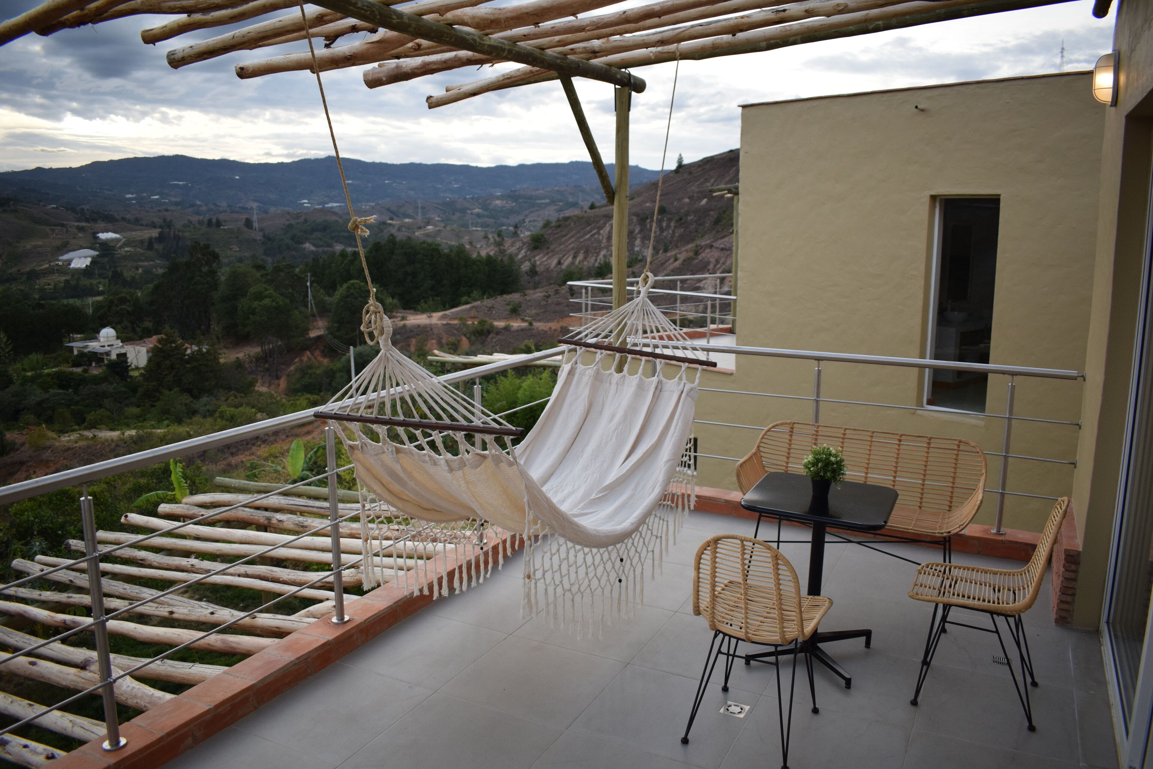 Un balcón con una hamaca, sillas de mimbre y una mesa con planta en maceta.