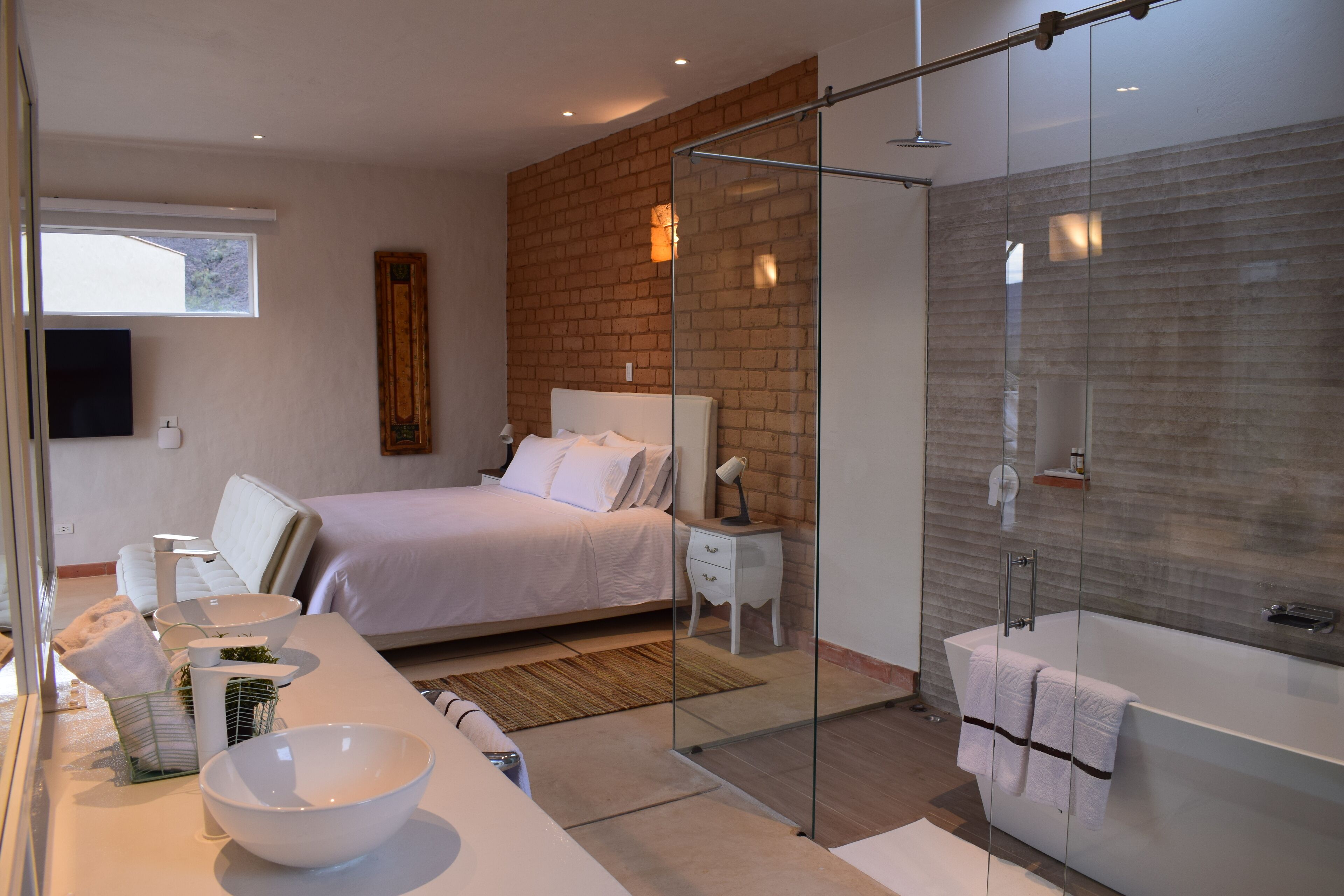 Un dormitorio moderno con una cama grande, cabina de ducha de vidrio y un baño con bañera y lavamanos.