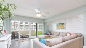 A modern living room with a beige sectional sofa, a ceiling fan, and a large window overlooking a balcony.