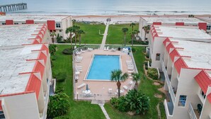 A hotel with a swimming pool, lounge chairs, and a view of the beach and ocean.