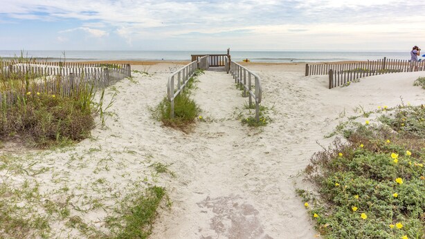 A sandy beach path leading to the ocean with a wooden fence and a gate.