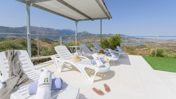 A covered outdoor seating area with white lounge chairs, towels, and flip-flops. - Jacaranda del Gastor by Ruralidays (Cádiz)