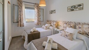 A hotel room with two beds, floral curtains, a view of the landscape, and a decorative wall piece. - Jacaranda del Gastor by Ruralidays (Cádiz)