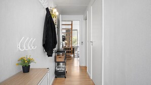 Käytävä, jossa on puulattia, takkihenkari, jossa on takki, viherkasvi ja koriin varustettu kärry.