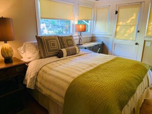 A bedroom with a bed, a nightstand, a lamp, and a window with blinds. - Now booking Fall/Winter- Charming Beach View Cottage (Laguna Beach)