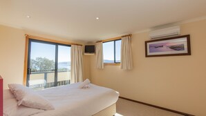 Un dormitorio con cama, televisor, ventana con cortinas, aire acondicionado y un cuadro enmarcado en la pared.