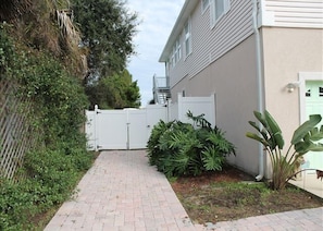 Stroll through lush gardens to a charming home with a white exterior and green door.