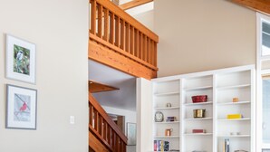 Una sala de estar con un sofá gris, estanterías blancas y una escalera de madera.