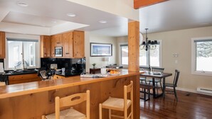 Una cocina moderna con armarios de madera, una isla central con taburetes de bar, un comedor con mesa y sillas, y una lámpara de araña.