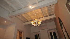 Ein Zimmer mit hoher Decke, einem Chandelier und einer Tür zu einem weiteren Raum.