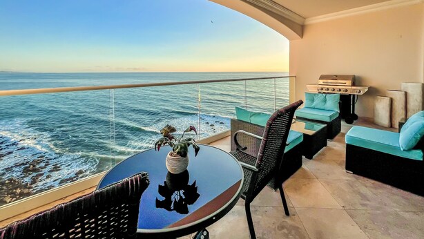 A balcony with a view of the ocean, a round table with a vase, and a grill. - Luxe&Stylish-LasOlasCondo-Pools&Jacuzzis-Rosarito (Rosarito)