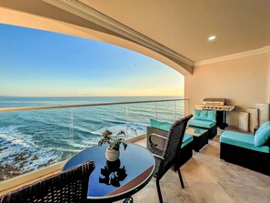 A balcony with a view of the ocean, a round table with a vase, and a grill.