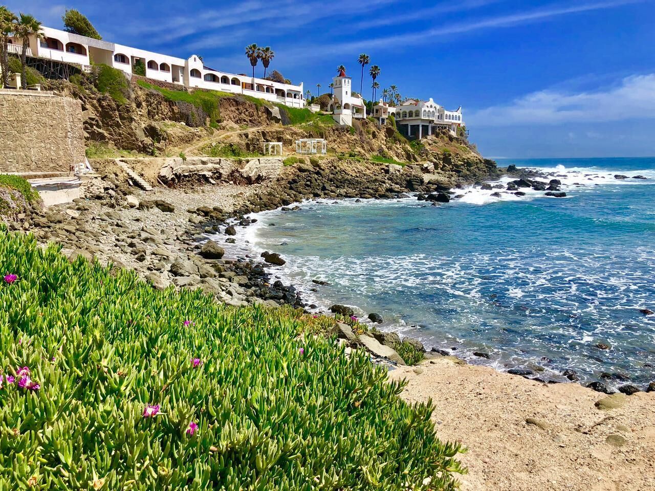 A coastal property with a rocky shoreline, a clear blue sky, and a building with multiple balconies overlooking the ocean.