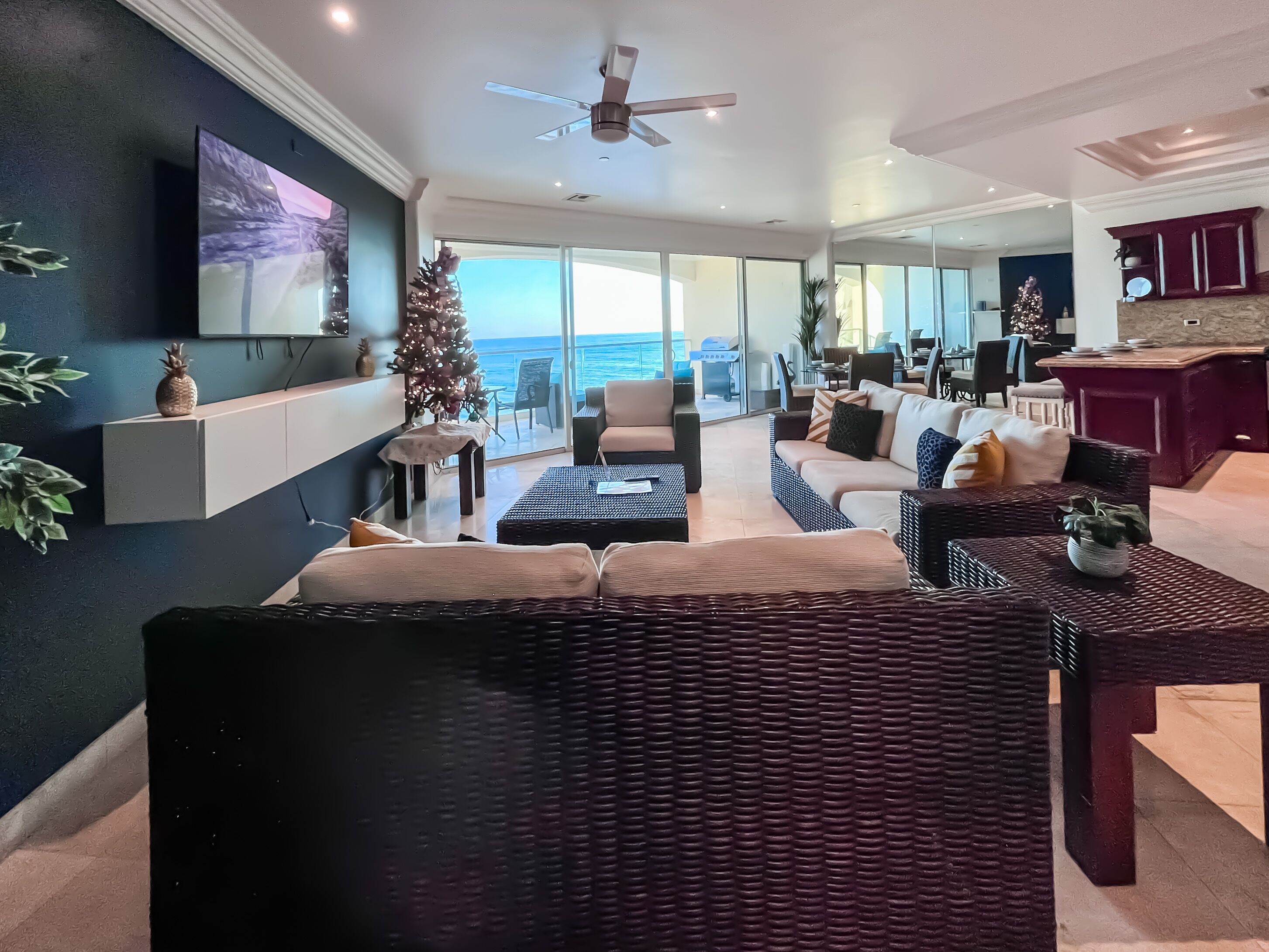 Un salon moderne avec un grand téléviseur, un sapin de Noël et une vue sur l’océan.