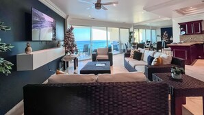 A modern living room with a large TV, a Christmas tree, and a view of the ocean. - Luxe&Stylish-LasOlasCondo-Pools&Jacuzzis-Rosarito (Rosarito)