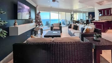 Un salon moderne avec un grand téléviseur, un sapin de Noël et une vue sur l’océan.