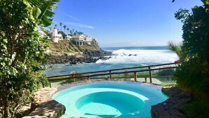 A swimming pool with a view of the ocean and a cliffside building. - Luxe&Stylish-LasOlasCondo-Pools&Jacuzzis-Rosarito (Rosarito)
