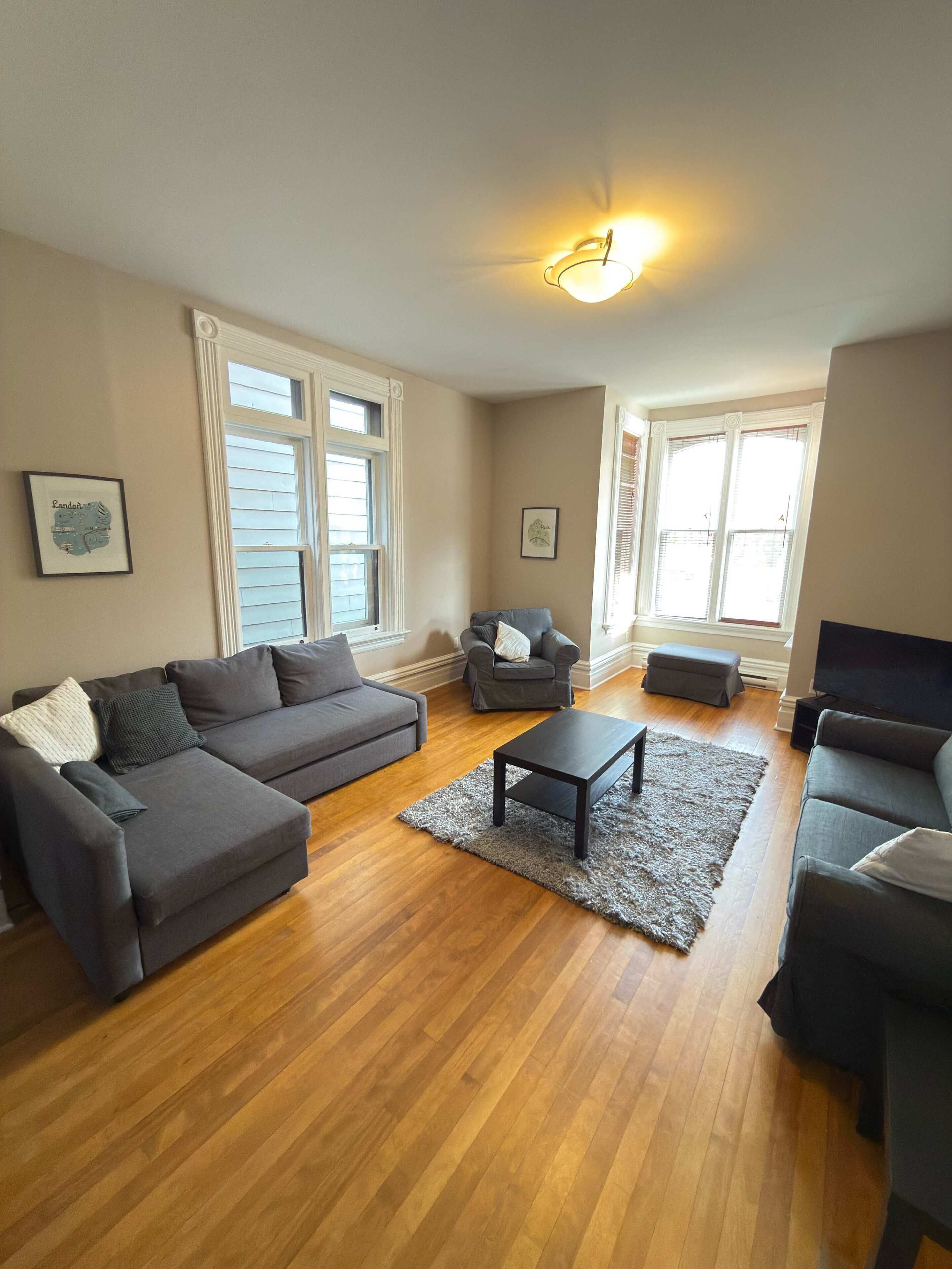 A living room with a grey sectional sofa, a grey armchair, a small ottoman, a coffee table, and a flat-screen TV.
