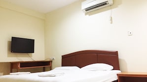 A hotel room with a bed, a television mounted on the wall, and an air conditioning unit.