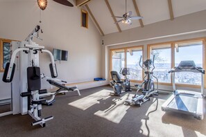 Une salle de sport équipée de divers appareils d’exercice, dotée de grandes fenêtres et d’un ventilateur de plafond.