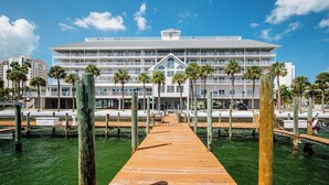 Un hotel frente al agua con un muelle de madera que conduce al edificio, rodeado de palmeras y agua.