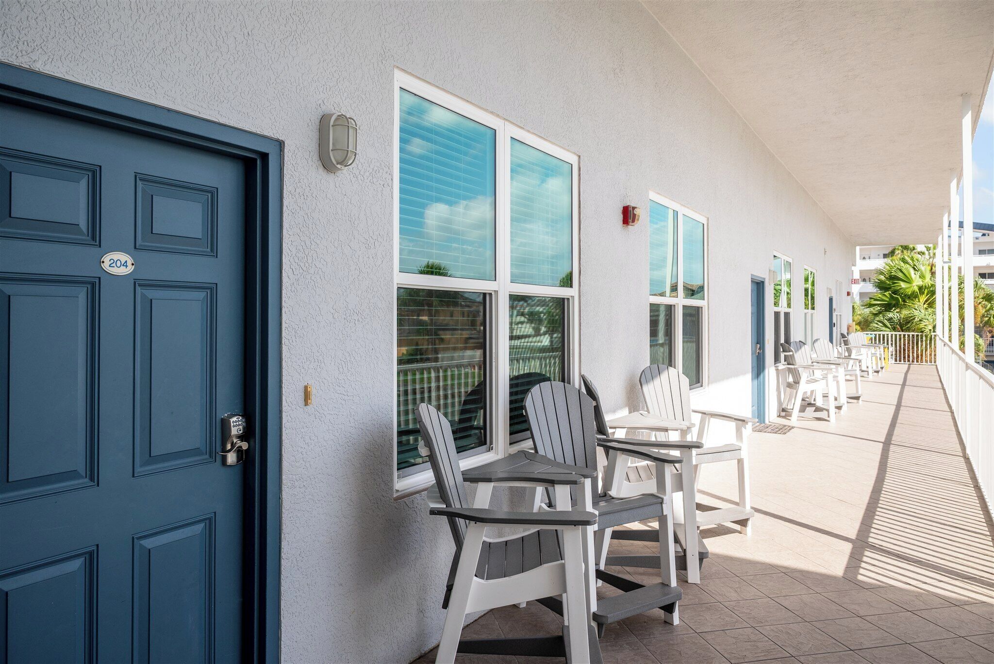 Un espace extérieur abrité, doté d’une porte bleue, de murs blancs et de plusieurs fauteuils Adirondack.