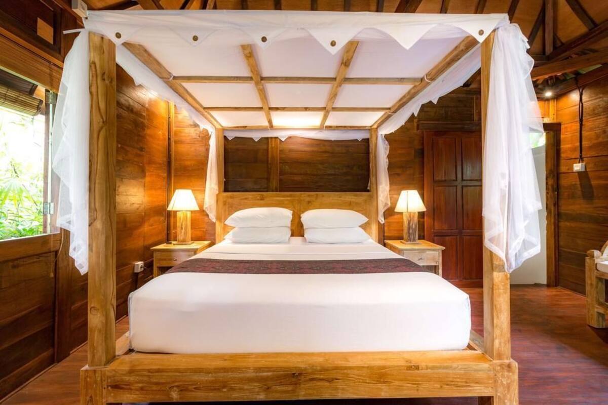 A wooden four-poster bed with white linens and two bedside lamps.