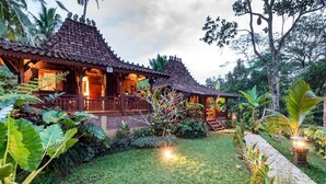 A traditional wooden house with a tiled roof, surrounded by lush greenery and a well-maintained lawn. - Be Bali Hut Farm Stay (Ubud)