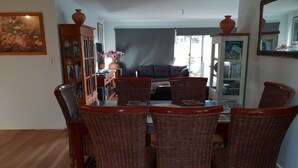 A dining area with a glass-top table surrounded by wicker chairs, a dark-colored sofa in the background, and a large mirror on the right. - Trading Places (Penneshaw)