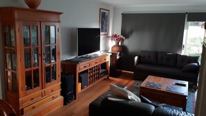 A living room with a wooden cabinet, a flat-screen TV, a sofa, and a coffee table. - Trading Places (Penneshaw)