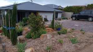 A residential house with a grey roof, a driveway, and a garden with various plants and rocks. - Trading Places (Penneshaw)