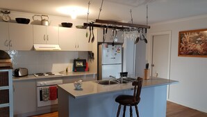 A modern kitchen with a central island, stainless steel appliances, and a hanging wine rack. - Trading Places (Penneshaw)