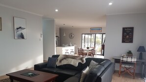 A modern living room with a black leather sofa, a wooden coffee table, and a dining area in the background. - Gilligan's Kangaroo Island (Baudin Beach)