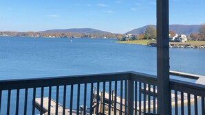 Une vue sur le lac depuis une terrasse dotée d’une rambarde en bois, avec un quai et des maisons en arrière-plan.