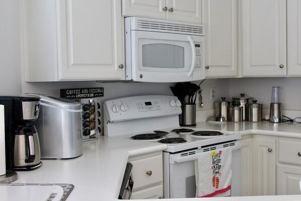 Una cocina con gabinetes blancos, microondas, estufa, cafetera y un letrero que dice "Coffee and Friends".
