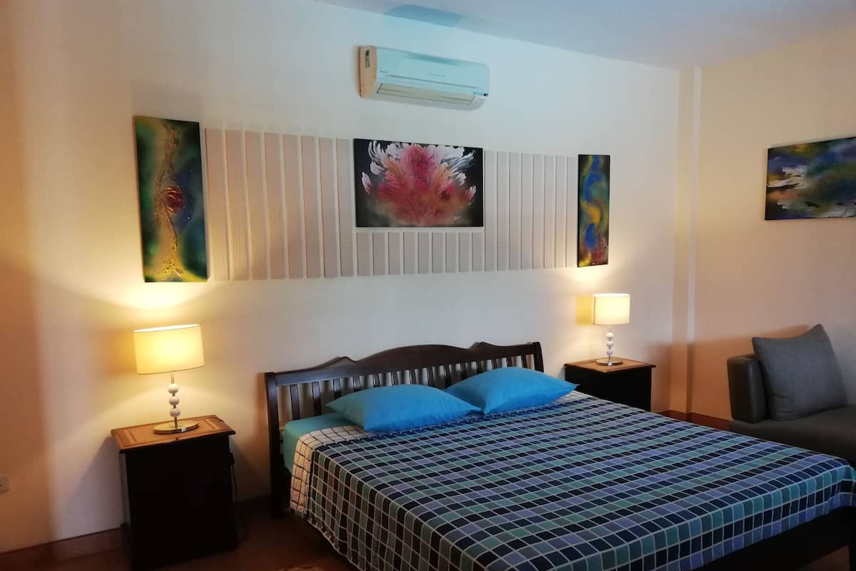 Une chambre à coucher comprenant un lit, deux tables de chevet, une commode, un climatiseur fixé au mur et deux lampes fixées au mur.