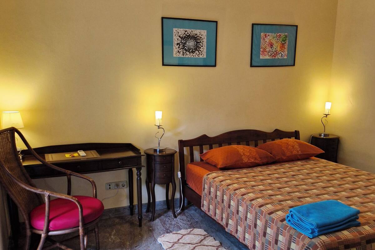 Une chambre d’hôtel comprenant un lit, un bureau, une chaise, deux œuvres d’art encadrées et un sol en marbre.