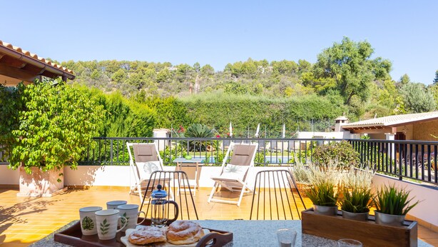 Eine Terrasse mit Außenbestuhlung, einem Tisch mit Gebäck und Blick auf eine Hügellandschaft.
