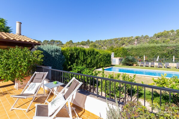 Une terrasse avec des chaises longues, une piscine et une vue sur la verdure et les collines environnantes.
