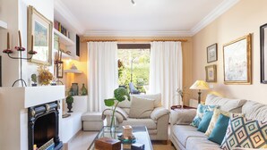 Ein gemütliches Wohnzimmer mit Kamin, einer Couch mit gemusterten Kissen, einem Couchtisch und einem Bücherregal.