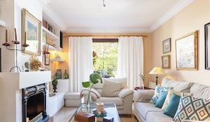 A cozy living room with a fireplace, a sofa with patterned cushions, a coffee table, and a bookshelf.