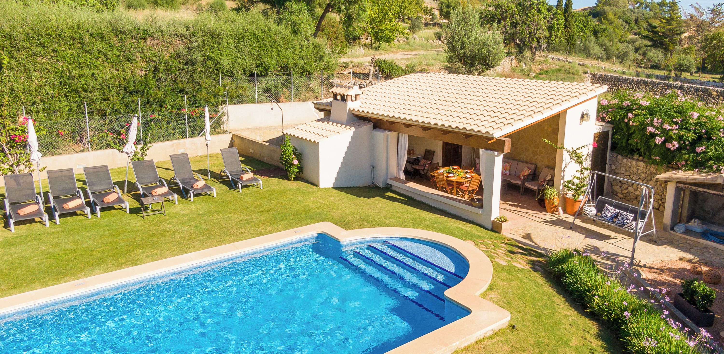 Una piscina con lettini, un patio con tavolo e sedie, e un muro di pietra sullo sfondo.
